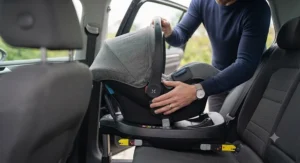 Close-up of a parent installing a travel system with car seat into a vehicle using an ISOFIX base.