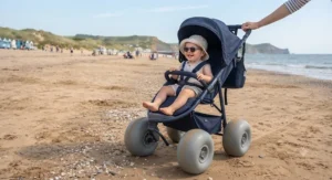 A happy toddler sitting in a beach stroller with sand wheels on a sunny day at a UK coastal resort