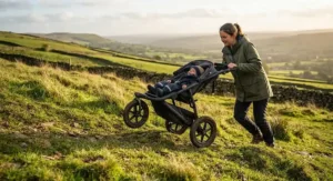 A parent pushing a sturdy pushchair for countryside walks up a grassy hill in the countryside.