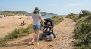 A parent pushing a toddler pushchair with heavy-duty sand wheels along a sandy coastal path