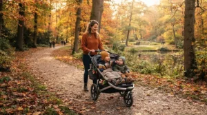 A pushchair for twins under £600 being wheeled along a paved path in a British park on a sunny afternoon.